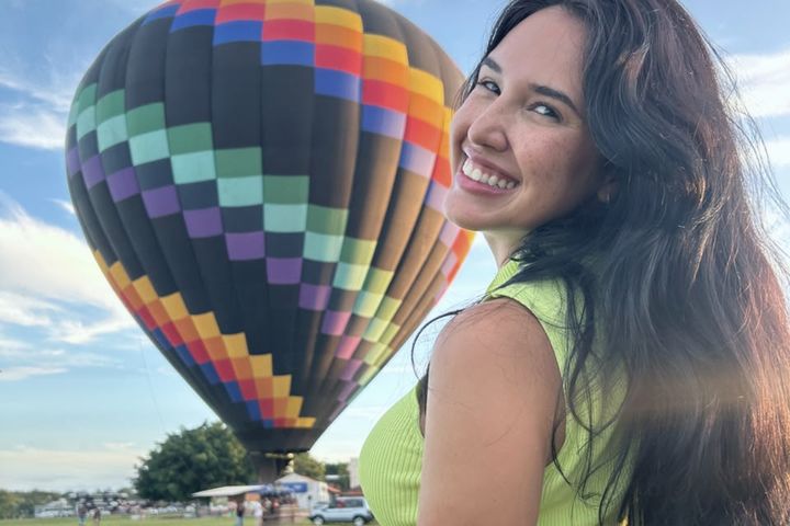 Passageira sorrindo ao lado do balão no campo de decolagem ao amanhecer