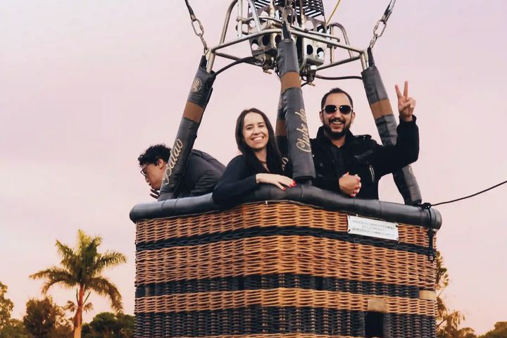 Casal no cesto do balão subindo contra o céu rosado do amanhecer